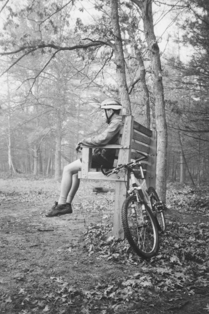 Mountain biker sitting on a high bench (intended for cross country skiers) on Muncie Lakes Pathway, near Traverse City, Michigan. 